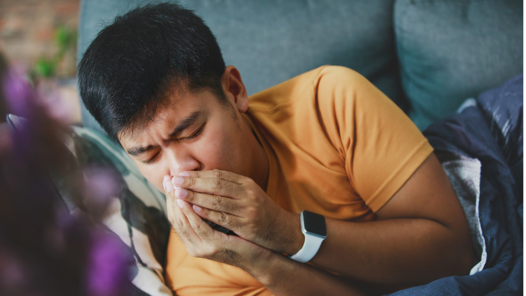 Man covering his mouth while coughing on a couch